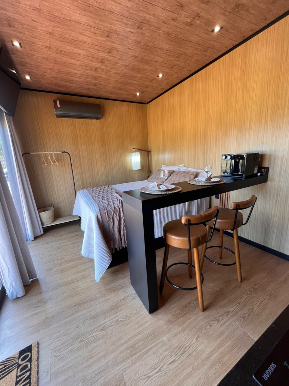 Vista ampla do interior com cama, bancada e cozinha em tons de madeira