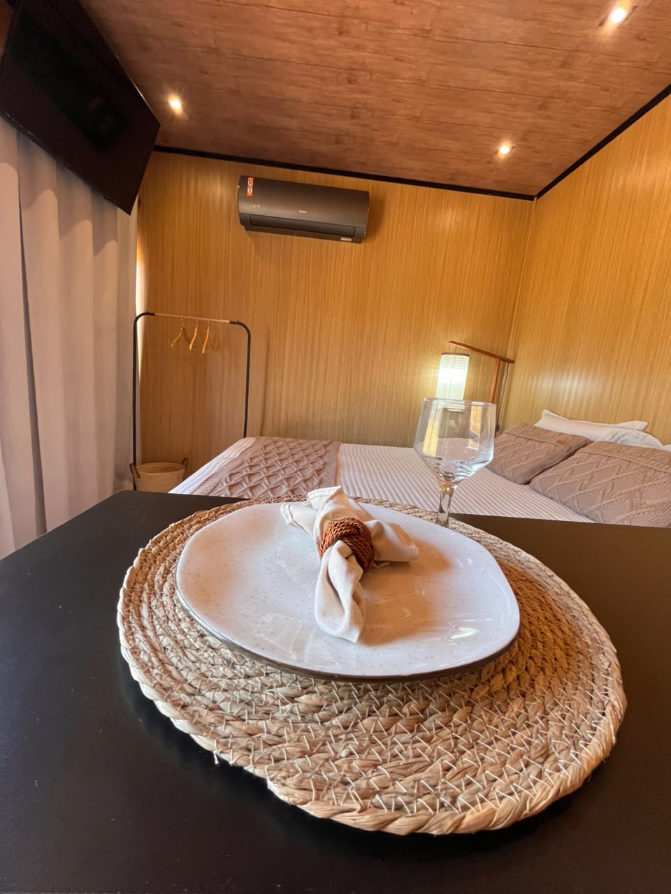 Prato e taça sobre sousplat de palha, com a cama ao fundo